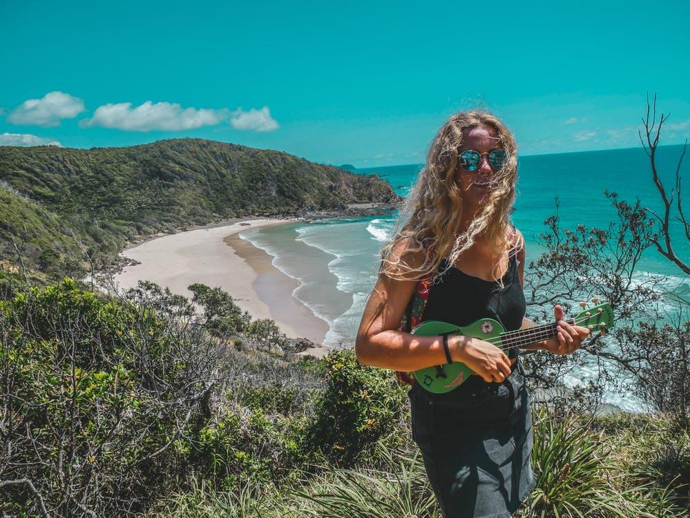 Woman Standing on Mountain While Playing Guitar Near Seashore